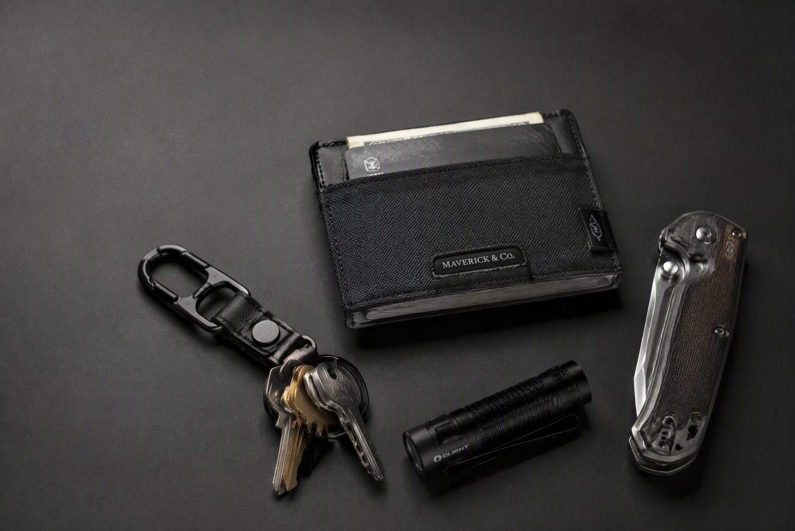 An EDC wallet clipped next to keys, a flashlight, and a multi-tool on a slate surface, moody lighting