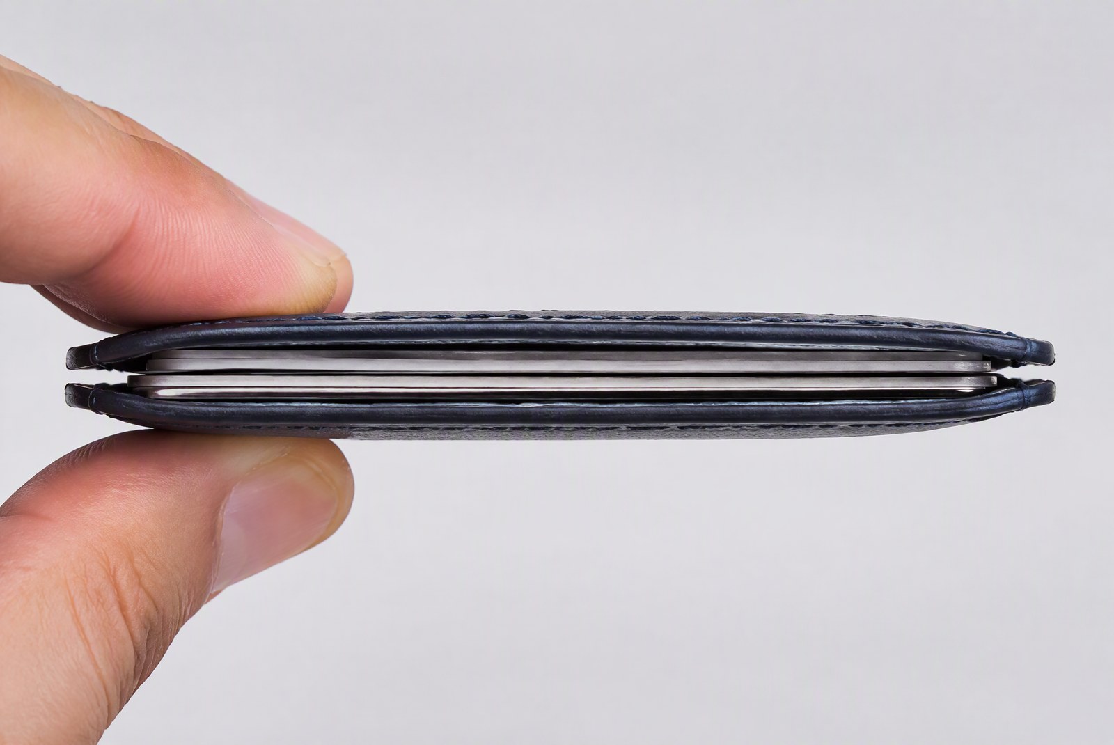 feature: factory-floor shot inside a wallet production line with aluminum plates, leather hides, and magnet assemblies on the bench, quality-inspection gloves in frame