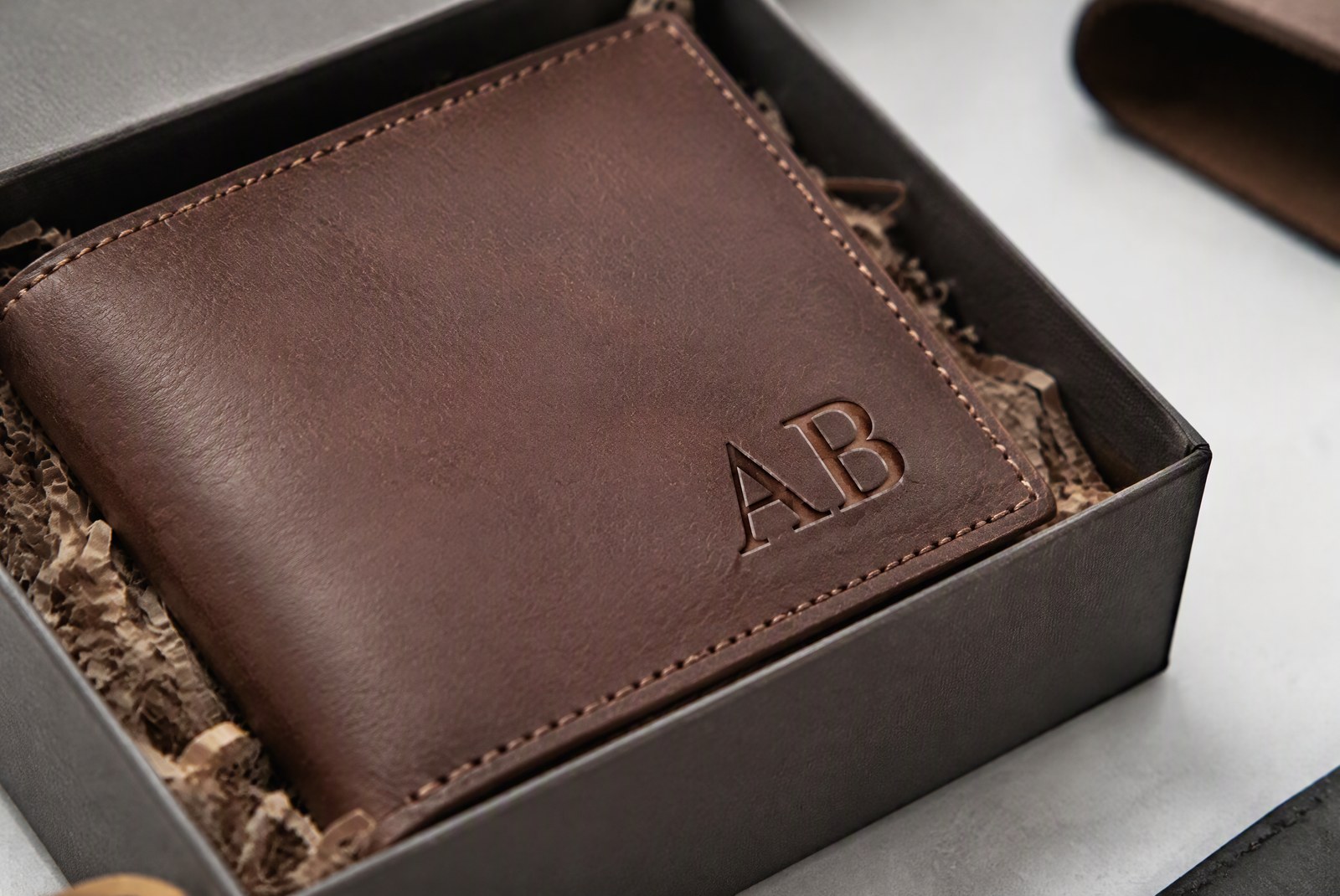 Manufacturer's finishing bench showing a laser engraving head in action over a metal wallet, with finished gift boxes stacked behind