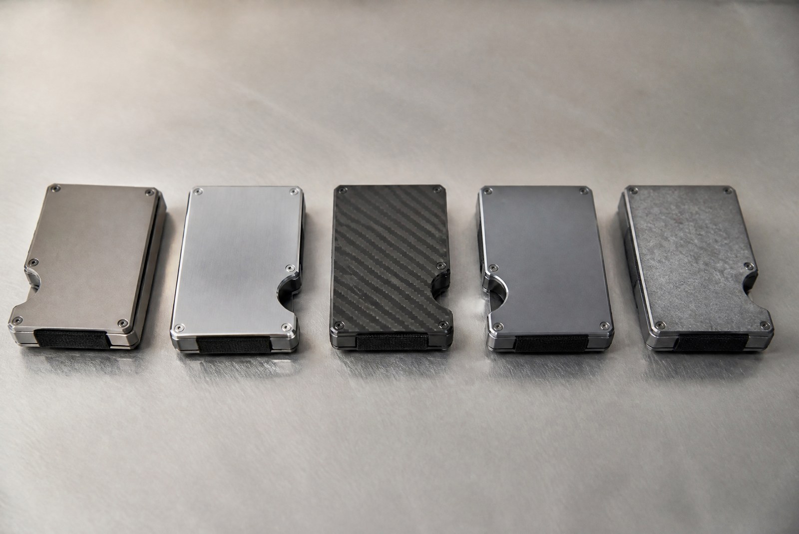 Metal wallets in aluminum, titanium, steel and carbon fiber arranged on a brushed metal surface