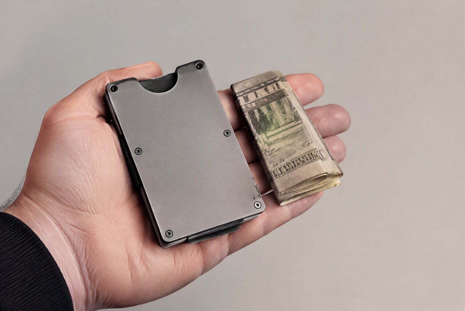 Hand holding a slim metal cardholder with cash folded beside it — the flat front-pocket profile