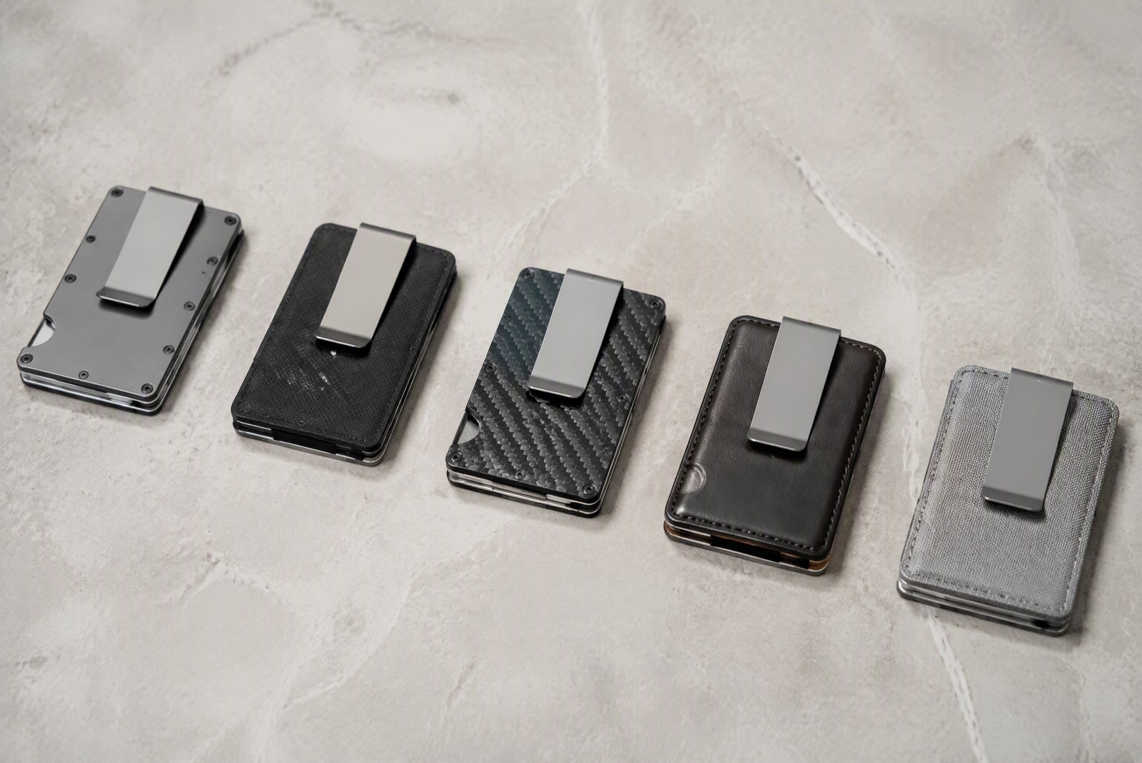 Money clip wallets in titanium, aluminum, steel and leather arranged on a light stone surface