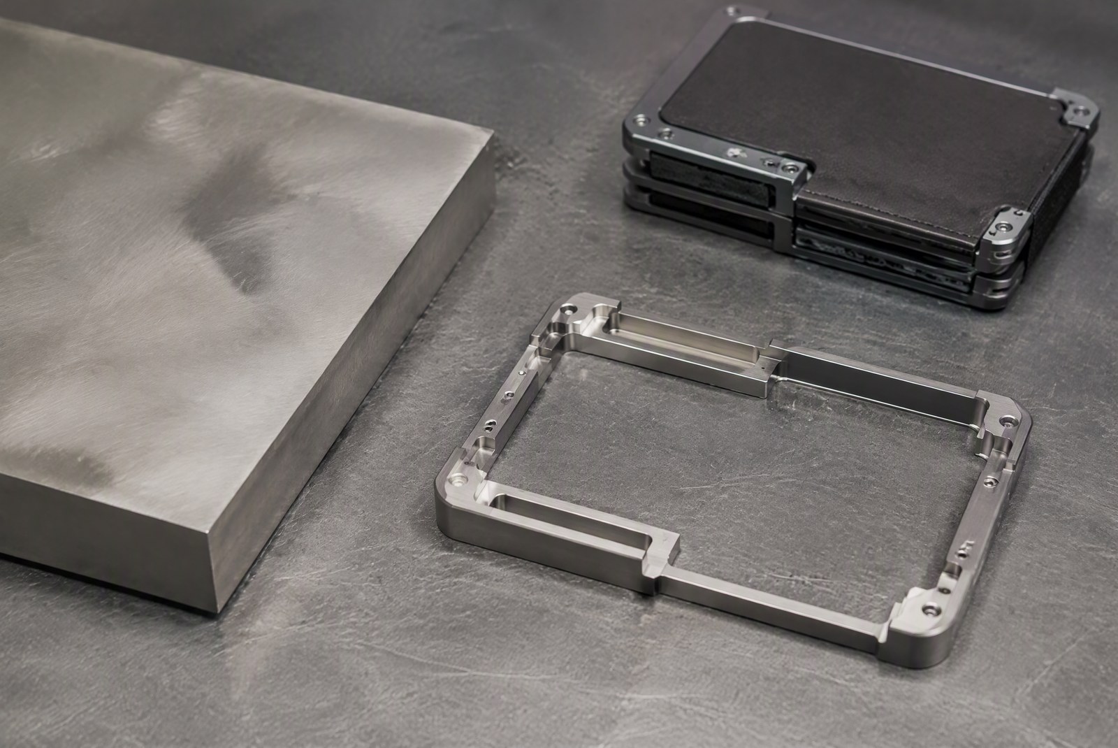 hero: macro product photography of a brushed grade 5 titanium card holder blank next to a bar of raw titanium stock, soft studio lighting showing the metal's natural gray tone